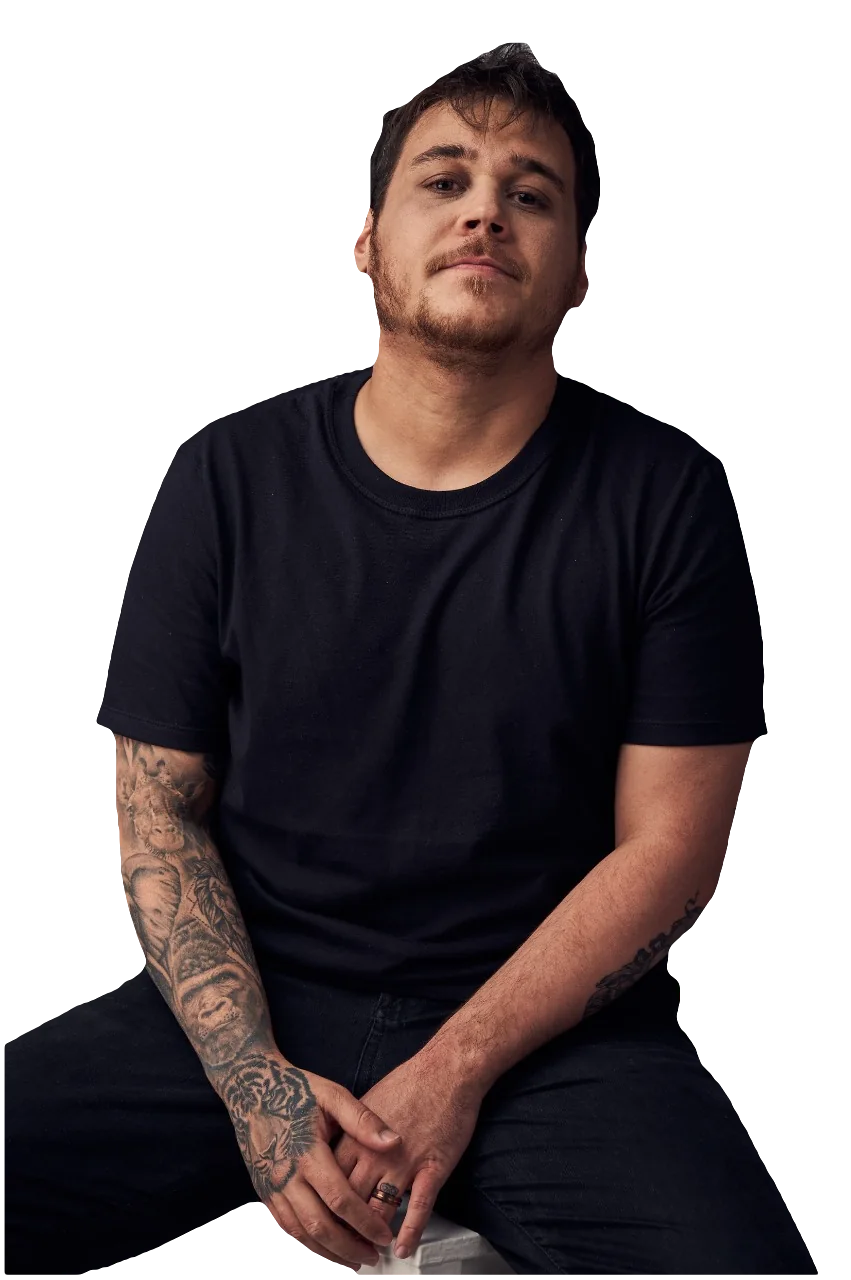 Mateus Lara apoiado em um banco, olhando para a câmera.
